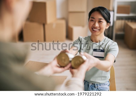 Portrait of smiling Asian woman volunteering at help and donations event, packing canned food in boxes, copy space Royalty-Free Stock Photo #1979221292
