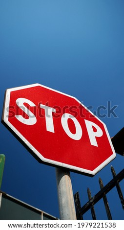Octagonal stop sign on a red background with fence and blue sky with clouds. conceptual photo
