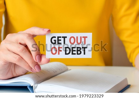 Get out of debt is written on a white business card. A woman's hand holds a white paper card against the yellow background. Business and advertising concept. Defocus.