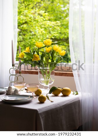 able setting by the open window. On the table is a vase with tulips, candles