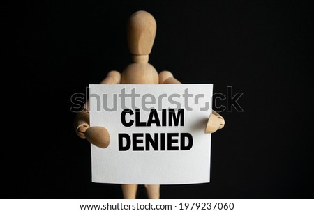 The wooden man holds a white sign with the text CLAIM DENIED in his hands. The content of the lettering has implications for business concept and marketing.