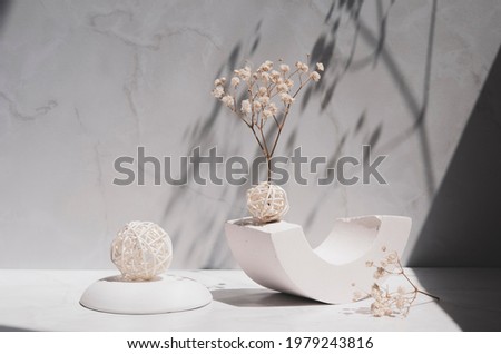 White geometric shape and podium, decorative balls and gypsophila flowers on a gray background. Modern interior still life with sunlight and shadows.  Royalty-Free Stock Photo #1979243816
