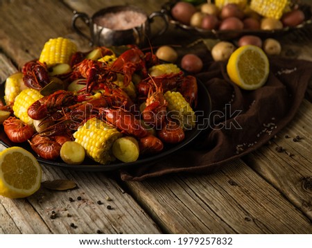 On a wooden table, a dish with boiled crayfish and pieces of corn. There is a sliced lemon next to it. Other ingredients in the background. Colorful photo. Close-up. There are no people in the photo.