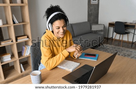 Young happy smiling African American adult student wearing headphones having virtual education class meeting online call e learning webinar on laptop at home office writing notes. Royalty-Free Stock Photo #1979281937