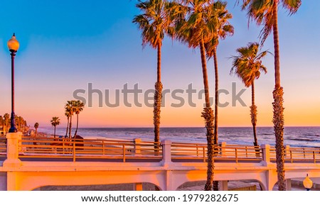 Oceanside Pier is surrounded by palm trees and sits on the edge of the Pacific Ocean in the golden light of sunset in Southern California.