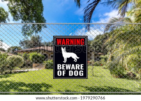A Beware of Dog Sign on a fence near a bungalow house. Warning to visitors or burglars. Security and protection in a residential home concept.