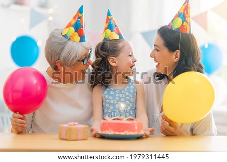 The kid is blowing out the candles on the cake. Grandmother, mother and daughter are celebrating birthday.