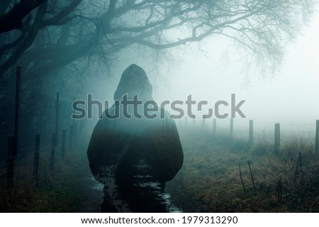 A double exposure of an atmospheric half transparent man looking at a foggy path in the countryside. On a moody foggy winters day.  Royalty-Free Stock Photo #1979313290