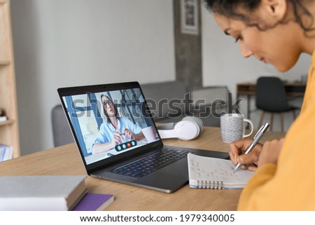 African American mixed race adult student having virtual meeting online call educational webinar chatting with senior teacher at home office writing notes. Video e learning conference call on pc. Royalty-Free Stock Photo #1979340005