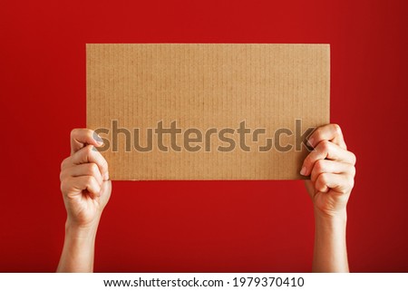 Hands holding a blank sheet of cardboard on a red background. Space for text Royalty-Free Stock Photo #1979370410