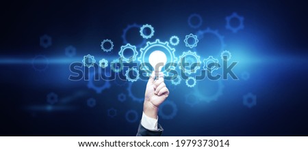 Creative idea and innovation concept with man hand carrying light bulb surrounded by digital gears on dark background