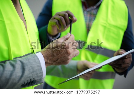 Mature engineer discussing the structure of the building with architects colleague at construction site. Signing document. Focus on hands.