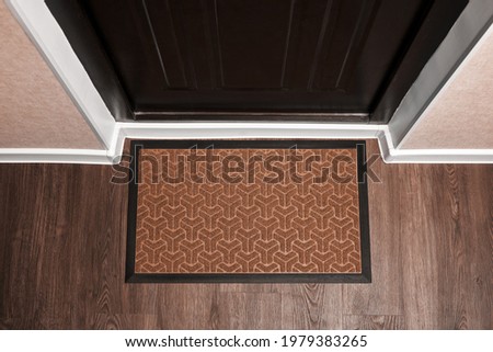 Blank doormat before the dark door in the hall. Top view of mat on wooden floor. Mockup for your design