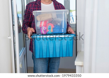 The man carries two plastic boxes with things, the upper transparent, the lower container is blue. Royalty-Free Stock Photo #1979433350