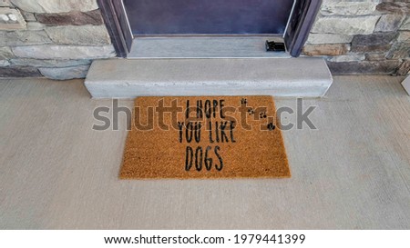 I hope you like dogs doormat at the doorstep of home with gray front door. Top view of the entrance of house with stone exterior wall.