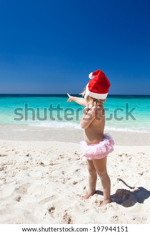 Cute little girl in Santa hat on white sandy beach