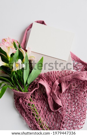 Feminine shopper bag with flowers and blank paper card on white background. Flat lay, top view.