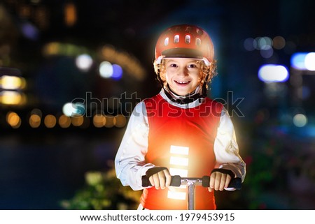 Kid in reflective vest in darkness. Safety on dark city streets for school children. Safe way home at night or in the evening. Fluorescent stripes on kids clothing and backpack. Boy walking at dusk. Royalty-Free Stock Photo #1979453915