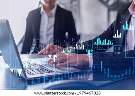 Two traders man and woman researching historic data to predict stock market behavior using laptop. Internet trading concept. Forex and financial hologram chart. Forecasting and planning.