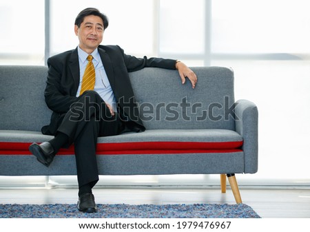 Portrait 60s Asian aged executive businessman wearing formal suit and necktie, sitting with smart self-confidence  and relax on the sofa in the comfortable office. successfully and proudly smiling Royalty-Free Stock Photo #1979476967