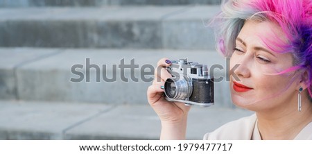 Caucasian woman with curly colored hair takes pictures on an old retro camera outdoors
