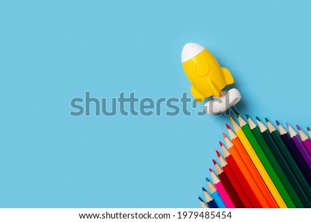 Back to school theme with colorful pencils and rocket on blue background flat lay, top view, copy space