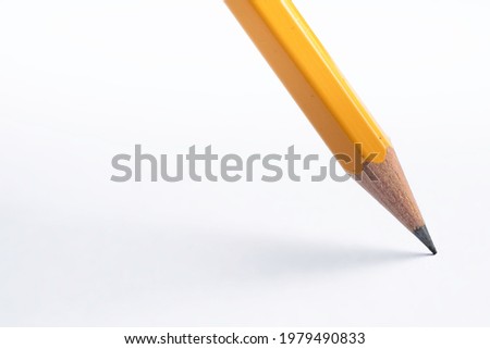 Pencil stands on white paper. The sharp point has just been sharpened. Focus on the black graphite tip. Background image