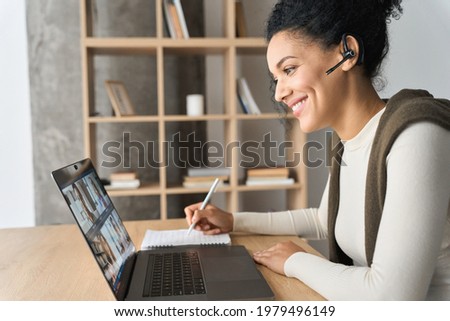 African American mixed race adult student wearing headset having virtual meeting online call educational webinar chatting at home office writing notes. Video e learning conference call on pc. Royalty-Free Stock Photo #1979496149