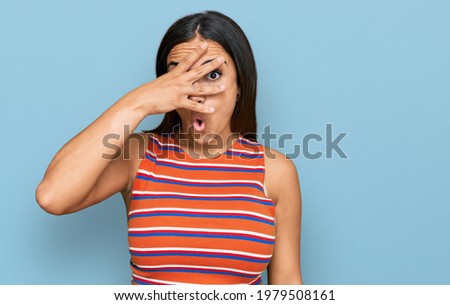 Young brunette woman wearing casual clothes peeking in shock covering face and eyes with hand, looking through fingers with embarrassed expression. 