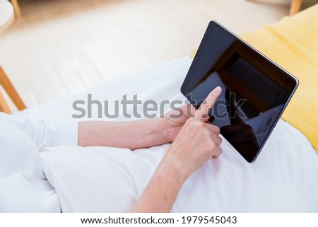 Closeup of senior woman's hand using tablet in the bed at home. Photo without face.