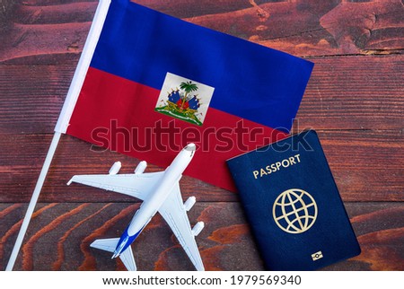 Flag of Haiti with passport and toy airplane on wooden background. Flight travel concept. 