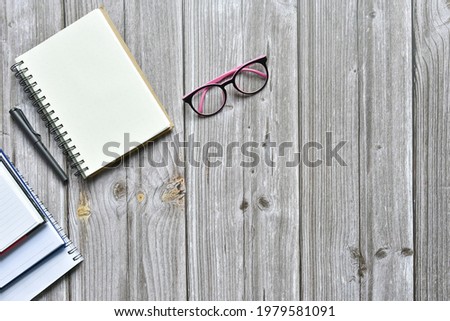 Still life, business office supplies or education concept, Top view image of open notebook and various colorful pencil and eyeglasses with blank pages on old brown wooden, ready for adding text