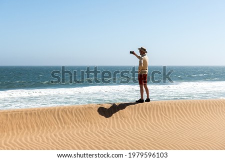 Single man in a cowboy hat takes a selfie in the Namib desert on Atlantic ocean background. Travel concept