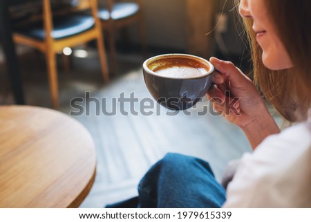 Closeup image of a beautiful young asian woman holding and drinking hot coffee