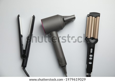 Hair dryer, straightener and triple curling iron on light grey background, flat lay Royalty-Free Stock Photo #1979619029