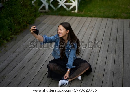 Happy Caucaisan vlogger smiling at front cellphone camera while shooting video for sharing to network web page, cheerful hipster girl using smartphone application for clicking selfie pictures