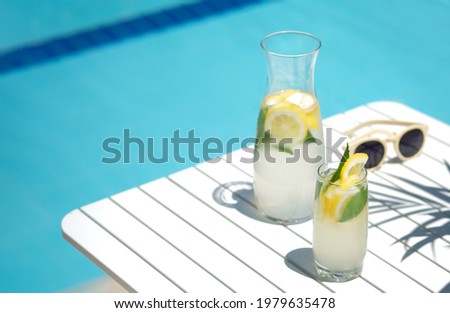 Homemade lemonade in glasses with lemon slice, on white table,in the edge of the pool with turquoise blue water background , light and shadows, vocation 2021 and summertime concept,space for text. Royalty-Free Stock Photo #1979635478
