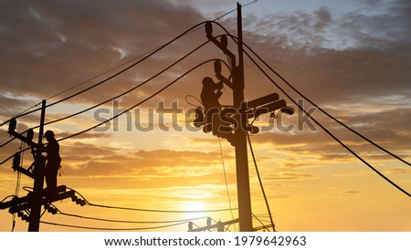 silhouette electricians work on high voltage towers to install new wires and equipment.