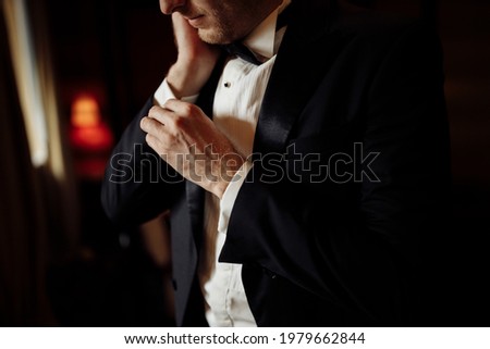 A close-up of a cropped frame of a man groom in an expensive classic costume and white shirt getting ready for event. The future husband is in a hurry and dressing up for wedding celebration. Royalty-Free Stock Photo #1979662844
