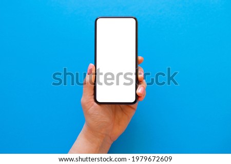 Person holding blank mobile phone in hand on blue background