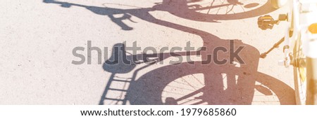 the gray shadow of a child's two wheeled bicycle or bike on the asphalt on a sunny day and part of a white bicycle. safe, socially distanced and active sports. banner. flare