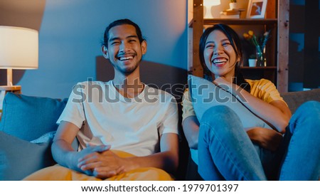Romantic asia couple man and woman smile and laugh lay down on sofa in living room at night watch comedy movie on television together at home. Married couple family lifestyle, stay at home concept. Royalty-Free Stock Photo #1979701397
