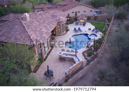 A high definition aerial view of a desert landscaped backyard with a pool, spa outdoor kitchen and fireplace.