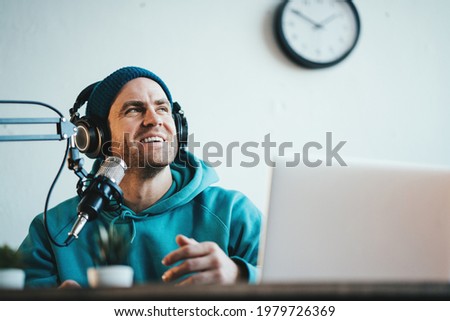 Cheerful host streaming his audio podcast at small and cozy home broadcast studio