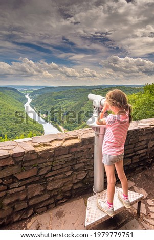 little girl in summer clothes using publice monocular telescope - young girl exploring beautiful surroundings of Saar river