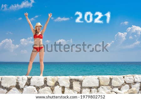 A beautiful woman in a swimsuit posing on a beach at summer. 2021 writen with clouds on sky.