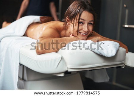 Adorable positive joyful woman looking at the photo camera while lying on massage table in spa salon