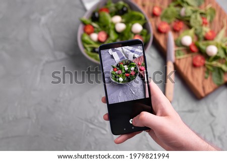 Man shooting fresh vegetable salad with mozzarella and spinach on cell phone camera. Cooking, blogging and healthy eating concept.