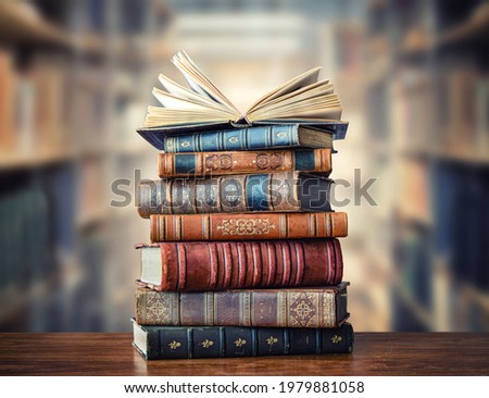 A stack of old books on table against background of bookshelf in library. Ancient books as a symbol of knowledge, history, memory and information. 
