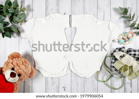 Baby wear two twins rompers onesie flatlay. On-trend farmhouse theme craft product mockup with farmhouse style decor, on a white wood background. Negative copy space for your design here. Royalty-Free Stock Photo #1979906054